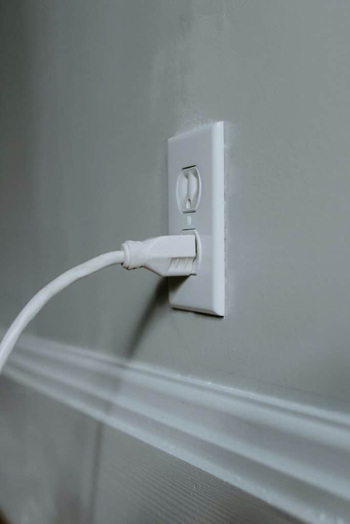 Power cord plugged into the bottom outlet of a two-outlet wall socket.