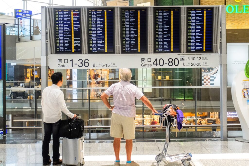 Two men stand looking at an airport screen of departures and arrivals.