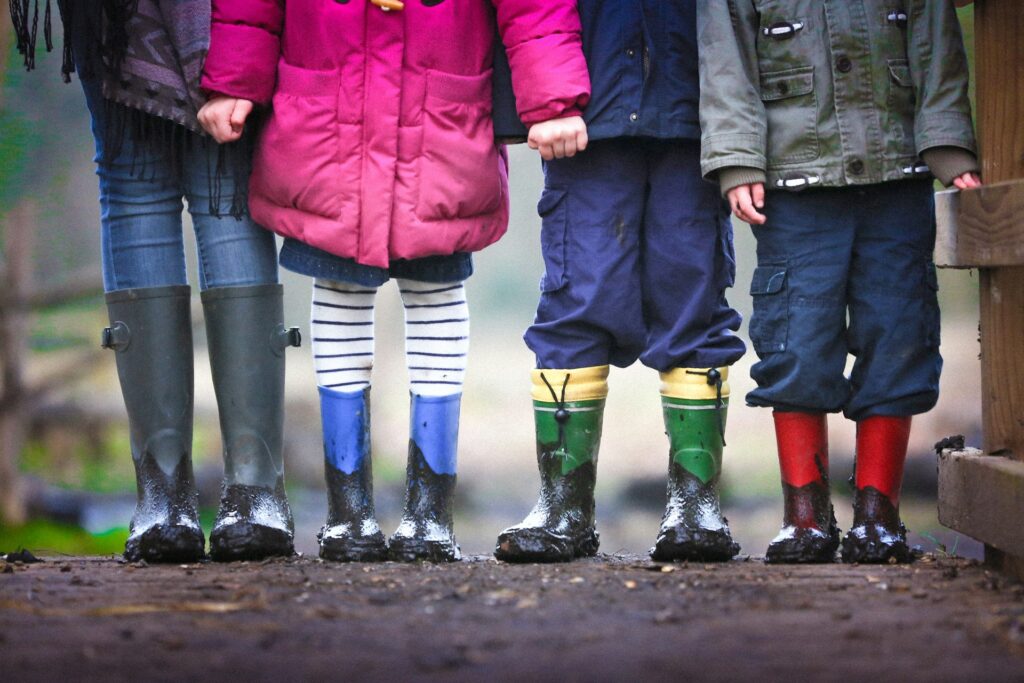 Kids standing in muddy rain boots.