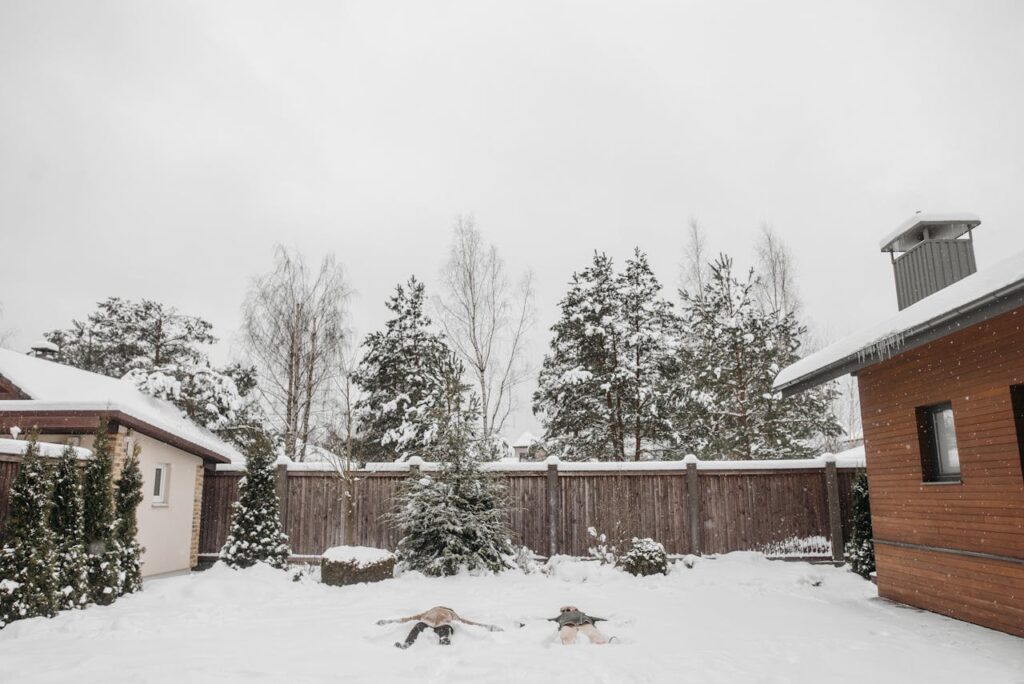 Two kids making snow angels in their suburban backyard.
