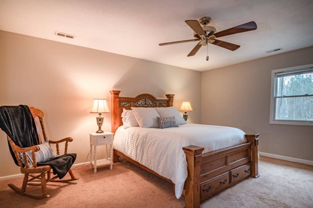 A guest bedroom with a queen size bed, ceiling fan, and rocking chair.