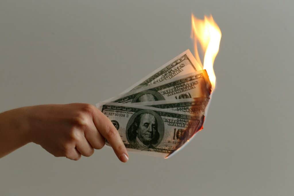 A woman's hand holding four 100 dollar bills that are on fire.