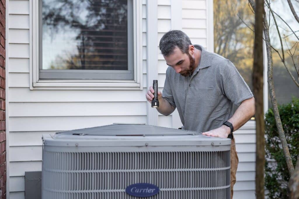 Technician evaluating a broken Carrier AC Unit outside of a home.