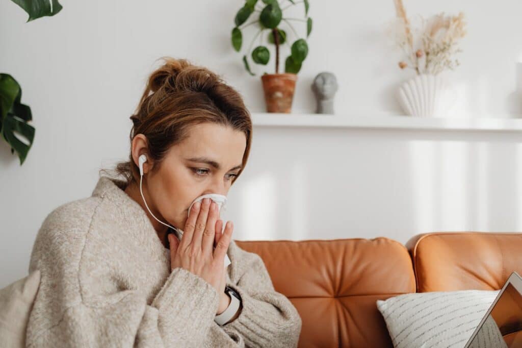 Woman blowing her nose inside due to indoor allergens