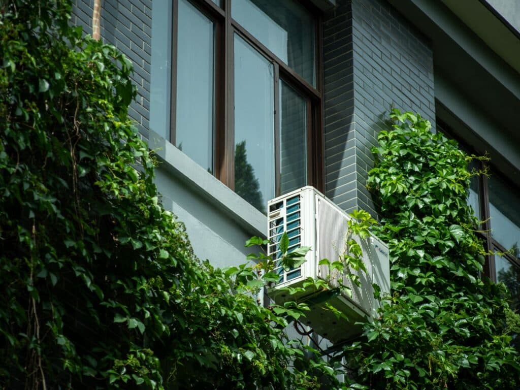Air conditioner with plants growing around it.